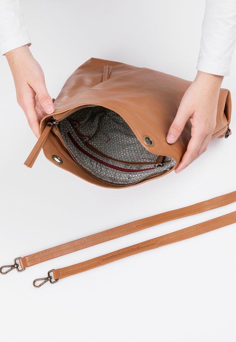 Braune Ledertasche mit einem Reißverschluss, die ein gemustertes Innenfutter zeigt. Mit zwei langen Lederträgern mit Metallclips und Branding-Detail.
