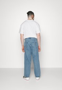 Baggy light blue jeans made of denim, paired with a plain white t-shirt. Visible back pockets with a small brand tag. White sneakers with black accents.