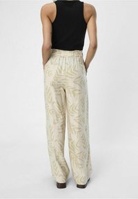 Løst siddende beige bukser med et diskret bladmønster, der har en elastisk talje. Bæres med en sort tanktop, der viser en afslappet pasform.