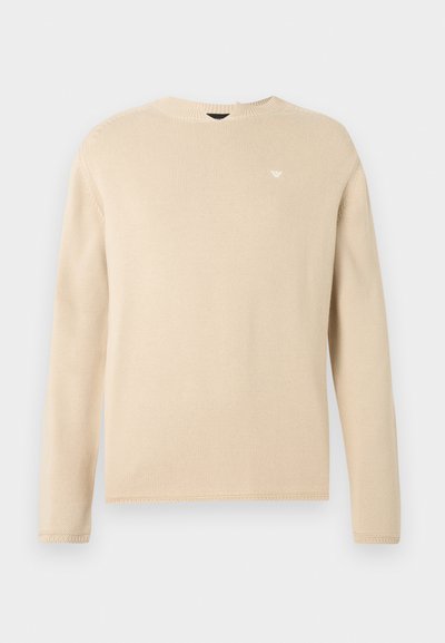 Pull en maille beige à manches longues avec col rond et petit logo blanc brodé sur la poitrine gauche, présenté sur un fond uni.