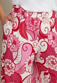 Blommönstrade byxor med stora rosa och röda blommor och virvlande blad mot en vit bakgrund; strukturerad tyg; elastisk midja.