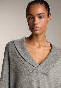 Maglione grigio lavorato a maglia con scollatura a V profonda e colletto a strati. Tessuto morbido, vestibilità comoda e maniche ampie. Tessuto liscio senza motivi.