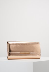 Cartera de mano metálica en color rosa dorado con una forma rectangular delgada, exhibida sobre un pedestal blanco contra un fondo claro y liso.