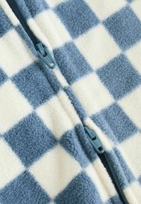 Fleecejacka med dragkedja i blå och krämfärgad rutig design. Mjuk textur med smidig dragkedja och matchande dragflik.