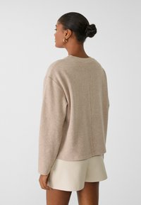 Beige wollen trui met een ronde halslijn, verlaagde schouders en een relaxte pasvorm. De mouwen zijn lang; de achterkant heeft een centrale naaddetail.