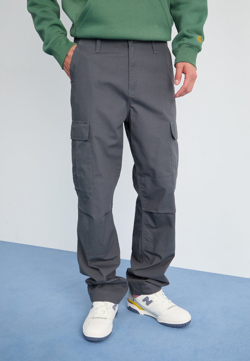 Pantalons cargo gris avec une finition texturée, plusieurs poches sur les côtés et une coupe décontractée, associés à des baskets blanches.
