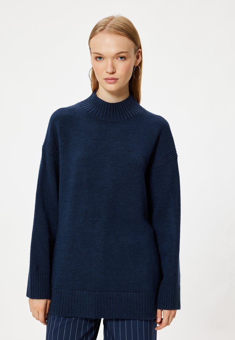 Maglione lavorato a maglia blu navy con girocollo alto a coste, spalle scese e polsini a coste. Vestibilità oversized con tessuto testurizzato.