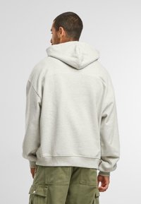 Lichtgrijze capuchon sweatshirt met een relaxte pasvorm, voorzien van een grote capuchon, geribde boorden en een soepele textuur. Gecombineerd met olijfgroene cargobroek.