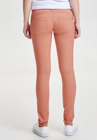 Jeans ajustados de color melocotón con una textura suave y dos bolsillos traseros. Con un diseño de cintura media y un corte a la altura del tobillo.
