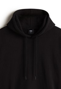 Sort hættetrøje med blød tekstur, der har en stor hætte, snore og et mærke syet ved halsudskæringen. Enkel og klassisk design.