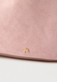 Surface en suède rose doux avec un petit logo en métal doré représentant des lettres entrelacées "A" et "F" près du bord inférieur.