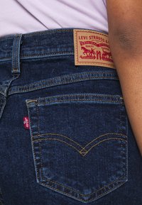Dark blue denim jeans with a visible leather patch labeled "Levi Strauss & Co." and a small red tag on the side pocket.