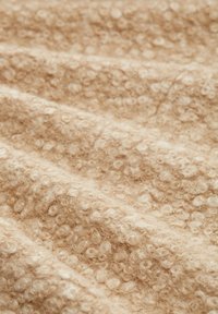 Beige strukturerad textil med mjuka, lockiga slingor och ett något skrynkligt utseende, vilket ger en taktil, plyschig yta.