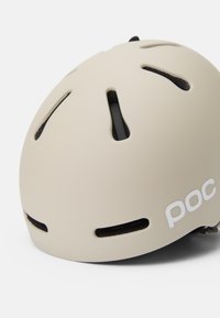 Futuristischer beiger Helm mit Belüftungsöffnungen und matter Oberfläche. Verfügt über ein schwarzes Innenfutter und ein auffälliges weißes Logo an der Seite.