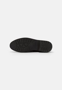 Semelle de chaussure en caoutchouc noir avec un motif de semelle texturé, présentant des rainures profondes et un design plat et durable pour une traction et une stabilité optimales.