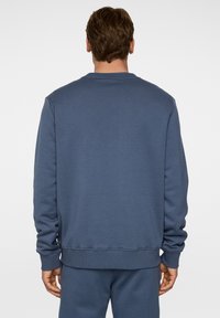 Sininen collegepaita pitkillä hihoilla ja ribbausväreillä. Ominaisuuksina pyöreä kaula-aukko ja rento istuvuus. Materiaali näyttää pehmeältä ja teksturoidulta.