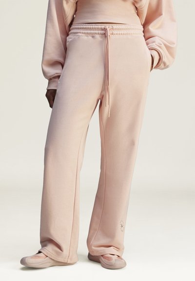 Light pink sweatpants with a drawstring waist, wide legs, and a soft texture. Features subtle logo detail on the lower hem.