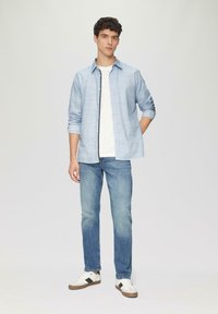 Jasnoniebieska koszula z guzikami na białym T-shircie, w połączeniu z jasnoniebieskimi dżinsami i białymi sneakersami z czarnymi akcentami.