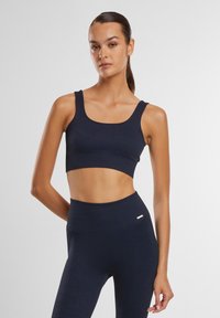 Mørkeblå ribbet crop top med brede stropper, parret med høyt liv ribbet leggings. Glatt tekstur og minimalistisk design.
