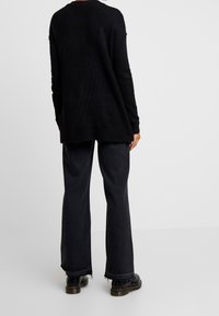 Svart stickad tröja med lös passform, ribbade ärmslut och rundad nederkant, tillsammans med mörka vida jeans och svarta kraftiga stövlar.