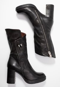 Par med svarta läderstövlar i midikort längd med klackar, en med synlig ytterblixtlås och den andra vikta med dekorativ spänne.