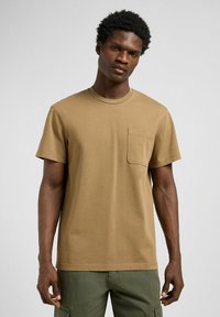 T-shirt di cotone color khaki con scollatura rotonda, maniche corte e una tasca sul petto. Tessuto morbido, vestibilità comoda e design semplice.