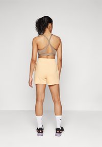 Brun sport-bh med racerback-design och utskärning, tillsammans med persikofärgade shorts. Ytterligare detaljer inkluderar svarta skor och vita strumpor.