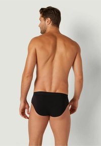 Schwarze Schwimmshorts mit niedrigem Schnitt, glatter Textur und elastischem Bund, von hinten an einem Modell gezeigt.