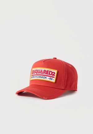 Casquette de baseball rouge avec un écusson bordé de jaune portant l'inscription "DSQUARED2 Born in Canada - 64" sur le devant, bords de la visière légèrement usés.
