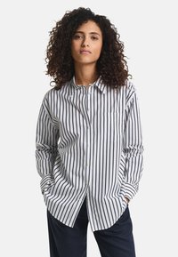 Gestreifte Hemdbluse in Weiß und Marineblau, mit einem klassischen Kragen, langen Ärmeln und einer Brusttasche, aus einem weichen Stoff gefertigt.