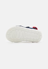 Sneaker med en hållbar vit gummisula, övre del i marinblå mesh och kontrasterande röda detaljer. Har en texturerad, mönstrad yttersula för bättre grepp.