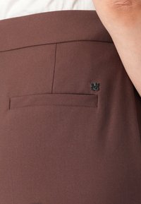 Bruine op maat gemaakte broek met een slanke silhoutte, textuurstof en een discreet logo-label bovenop een achterzak.
