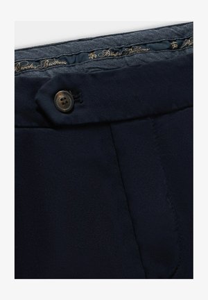 Donkerblauwe broek met een gladde textuur, een enkele bruine knoopsluiting en een decoratief etikettering op de tailleband met gouden tekst.