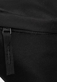 Borsa in tessuto nero con superficie strutturata, dotata di zip e di una tracolla robusta, adatta per trasportare oggetti personali o attrezzature.