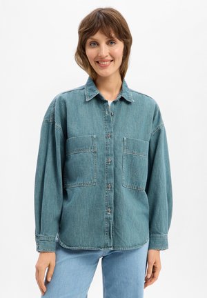 Turquoise spijkerblouse met een knoopsluiting aan de voorkant, twee grote borstzakken en lange mouwen. Casual pasvorm met een iets oversized silhouet.