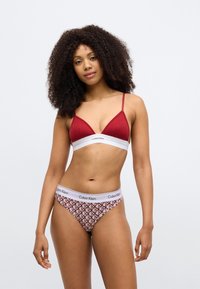 Červená rebrovaná trojuholníková podprsenka s bielym pásom; zodpovedajúce bikiny s geometrickými tvarmi v červenej a bielej farbe. Elastický materiál, priliehavý strih.