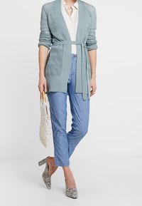 Ljusblå stickad kofta med knytbälte, kombinerad med ljusblå linneblandade byxor. Mönstrade grå klackar och en nätväska.