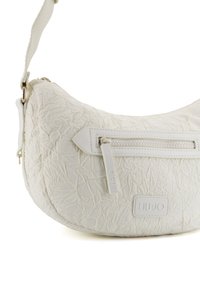 Borsa bianca con texture stropicciata e forma curva, dotata di una tasca con zip frontale e logo impresso su un patch rettangolare. Tracolla regolabile.