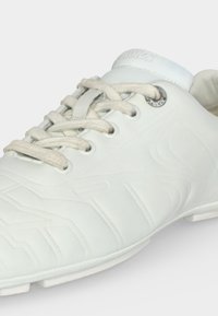 Baskets basses blanches avec motifs géométriques en relief, lacets blancs passant dans des œillets métalliques, et languette et col rembourrés.