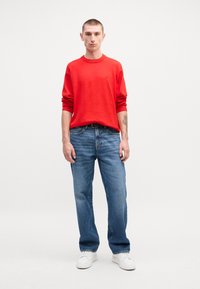 Červený pulóver s okrúhlym výstrihom, skombinovaný s svetlomodrými rovnými džínami. Biele tenisky dokončujú outfit. Jednoduchý dizajn, voľný strih.
