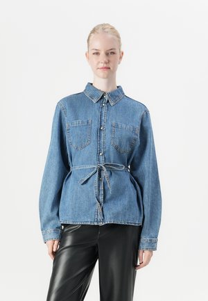 Denim shirt in light blue with a classic collar, two breast pockets, and a tied waist. Long sleeves with button closure and contrasting stitching.