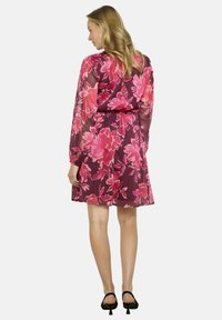 Vestido floral transparente con mangas largas, que presenta grandes flores rosas y rojas sobre un fondo burdeos. Con cinturilla ajustada y longitud por encima de la rodilla.