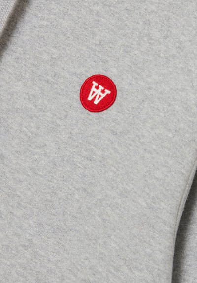 Grauer Stoff mit einer weichen Textur, gekennzeichnet durch einen roten runden Patch mit weißem "W"-Schriftzug. Minimalistisches Design, ohne zusätzliche Muster oder Akzente.