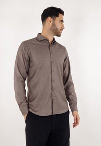 Brun teksturert langermet skjorte med knapper foran og spiss krage, kombinert med svarte bukser. Enkel, ren design.