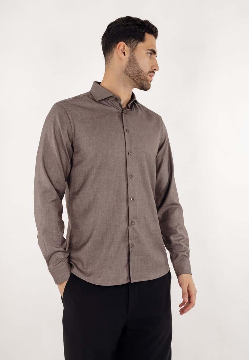 Brun teksturert langermet skjorte med knapper foran og spiss krage, kombinert med svarte bukser. Enkel, ren design.