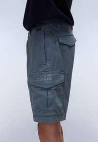 Men's cargo shorts in slate blue, featuring a relaxed fit, multiple pockets, and a stitched logo on the side pocket. Smooth fabric texture.