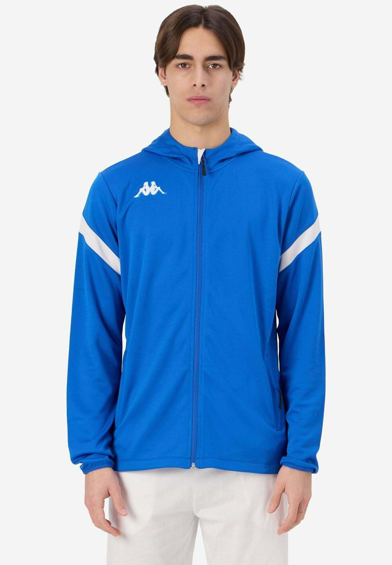 Giacca sportiva blu con cappuccio, realizzata in tessuto liscio, con strisce diagonali bianche e un piccolo logo sul petto. Chiusura frontale con zip.