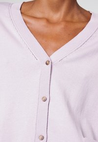 Lavender cardigan with a V-neckline, ribbed texture, and decorative button details along the front, showcasing a soft, knitted fabric.