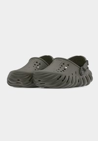 Paire de sabots gris sans lacets avec des trous de ventilation et des semelles sculptées en forme de vagues avec des sangles de talon réglables.