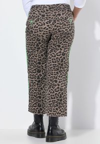 Korte broek met leopardprint en groene ster borduursels op de achterzakken, gedragen met zwarte veterschoenen en een witte top.